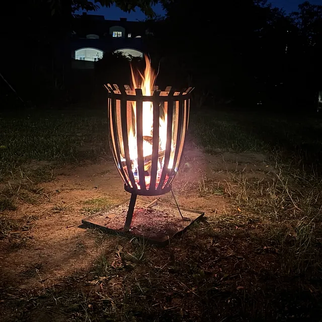 ein Feuerkorb mit Lagerfeuer, es beleuchtet nur den Boden rundherum, sonst ist es dunkel